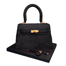 Load image into Gallery viewer, Hand-sculpted black Kelly-style handbag cake with realistic edible details by Bal Cakery, London.