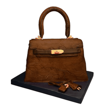 Load image into Gallery viewer, Hand-sculpted brown Kelly-style handbag cake with realistic edible details by Bal Cakery, London.