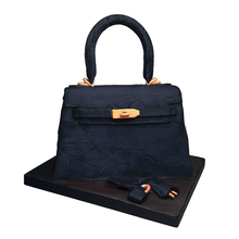 Load image into Gallery viewer, Hand-sculpted navy Kelly-style handbag cake with realistic edible details by Bal Cakery, London.